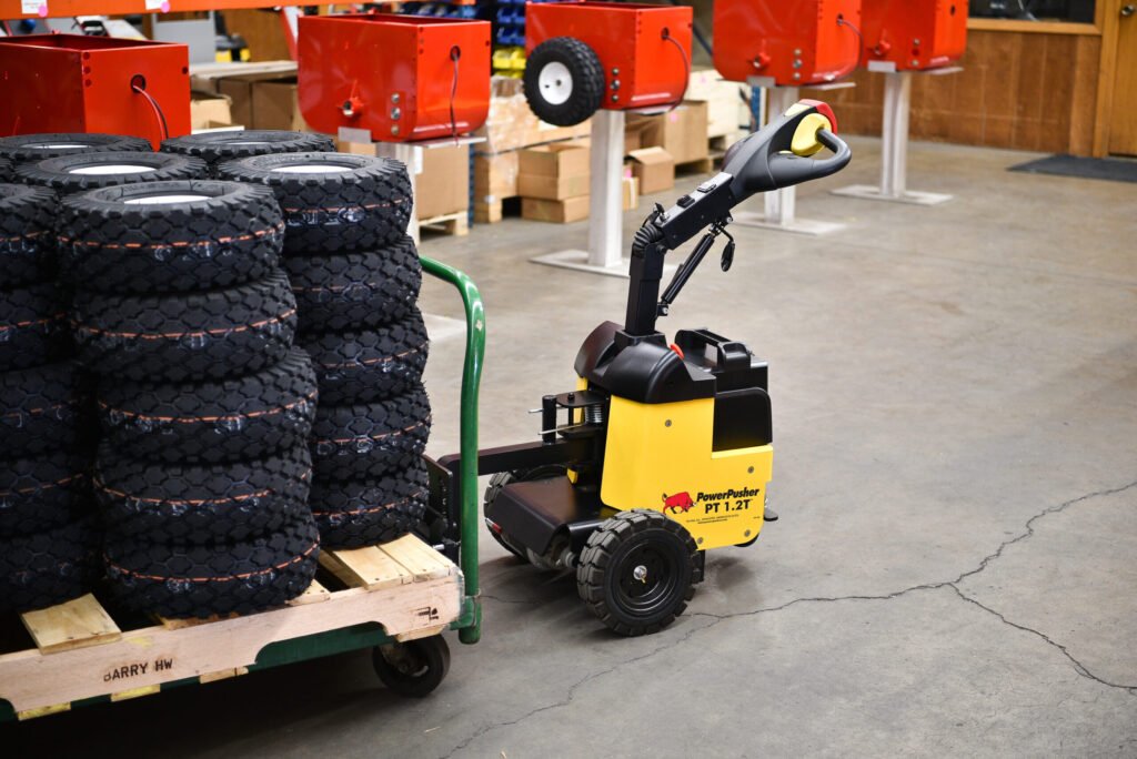 PT 1.2T™ electric tug transporting stacked boxes through a warehouse aisle​